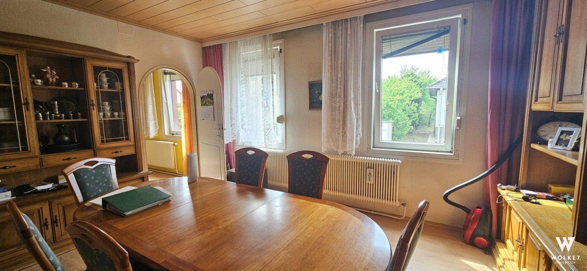 Esszimmer mit großem Holztisch, Vitrinenschrank und Fenstern für viel Tageslicht.