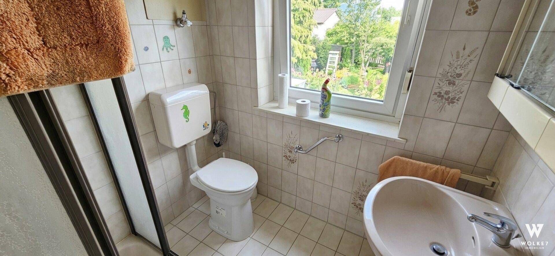 Helles Badezimmer mit Fenster, Dusche, WC und Fliesen in hellem Beige.