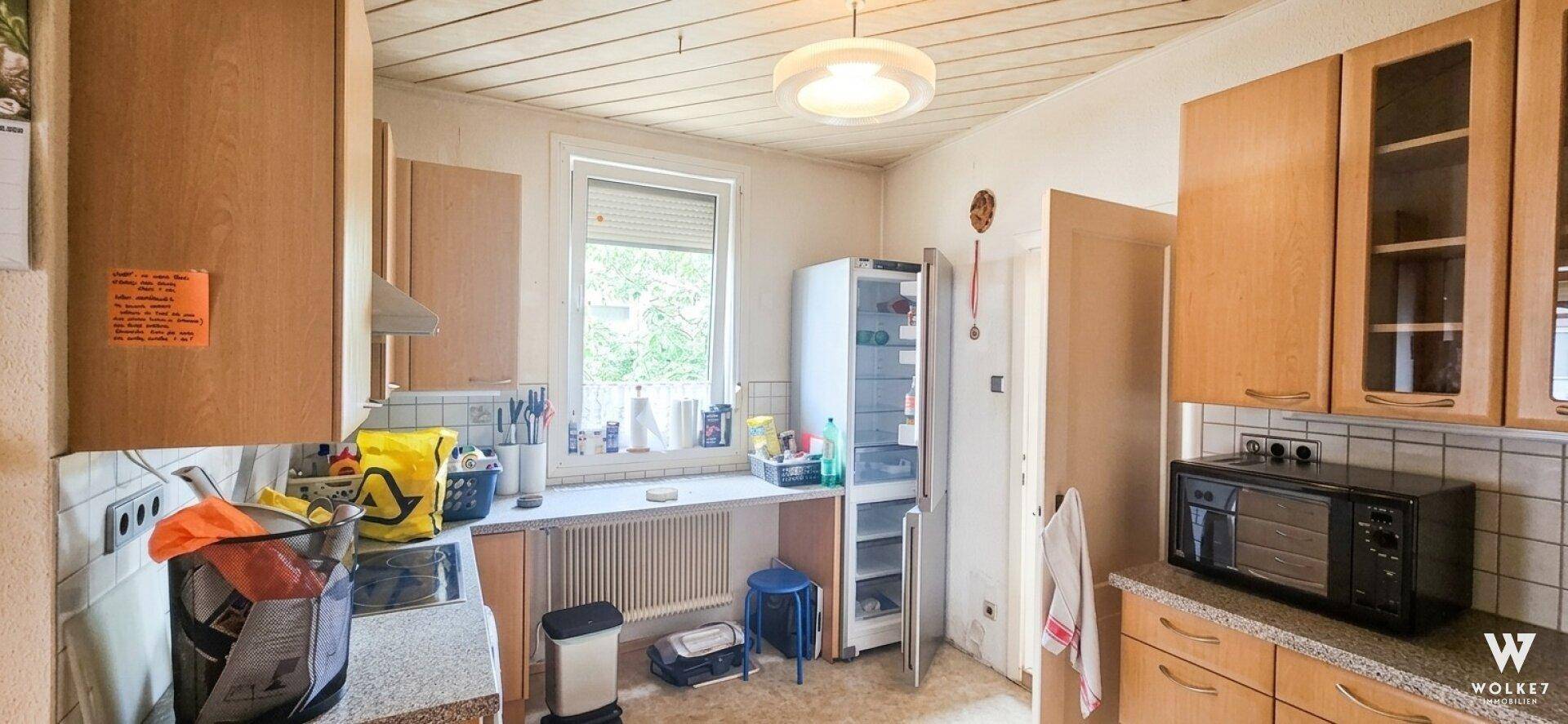 Funktionale Küche mit Holzschränken, Fenster und grundlegenden Geräten.