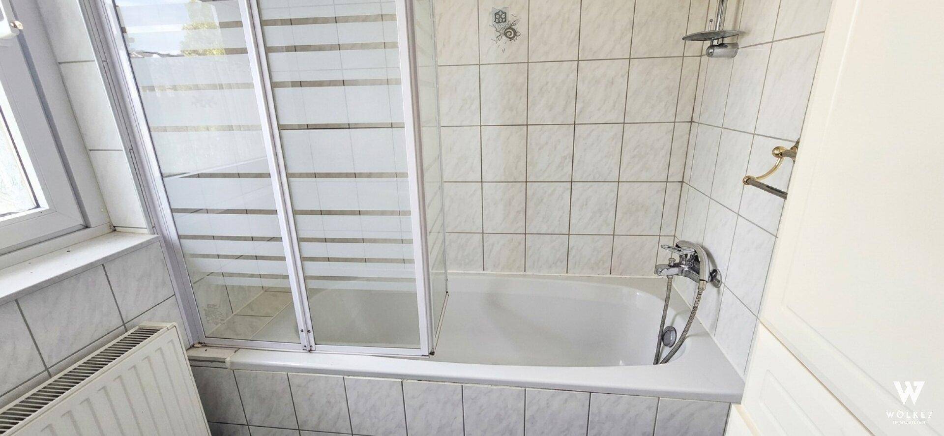Badezimmer mit Badewanne und Duschabtrennung, gefliest in hellem Beige.