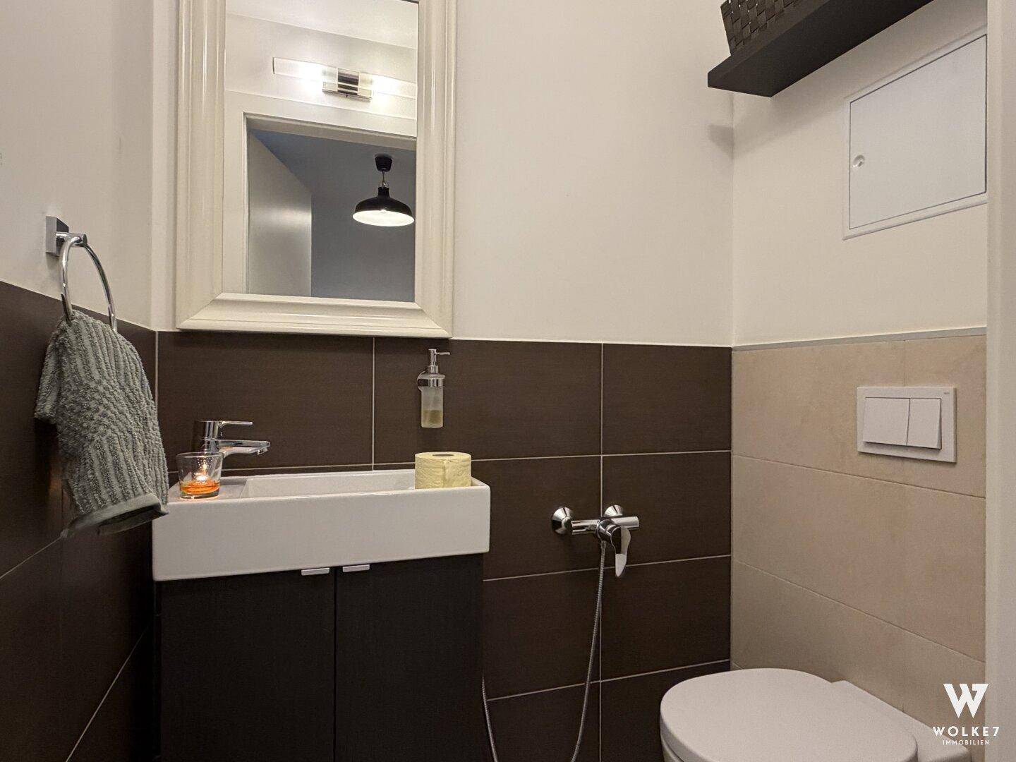 Kleines Gäste-WC mit modernem Waschtisch, Wand-WC und zweifarbigen Fliesen an den Wänden.