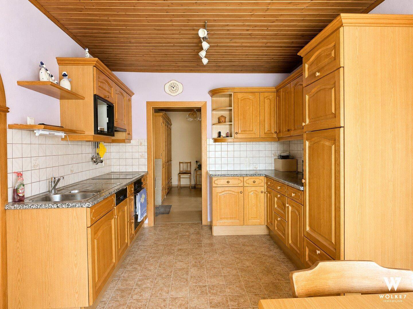 Funktionale Küche mit Holzschränken, Fliesenboden und Blick in den Flur.