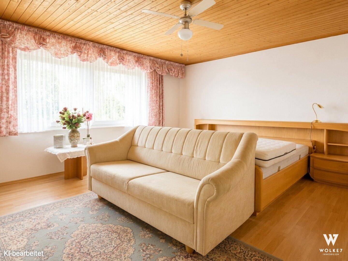 Schlafzimmer mit Doppelbett, Sofa, Holzdecke und großem Fenster.