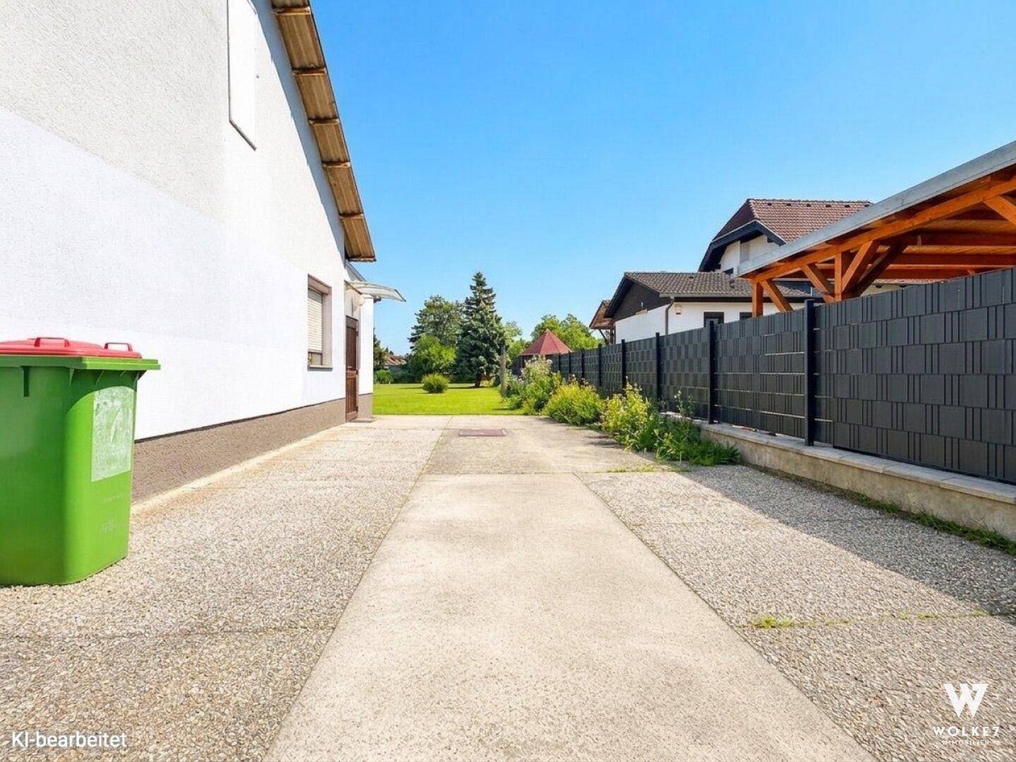 Lange Einfahrt zum Grundstück mit Zaun und Grünflächen.