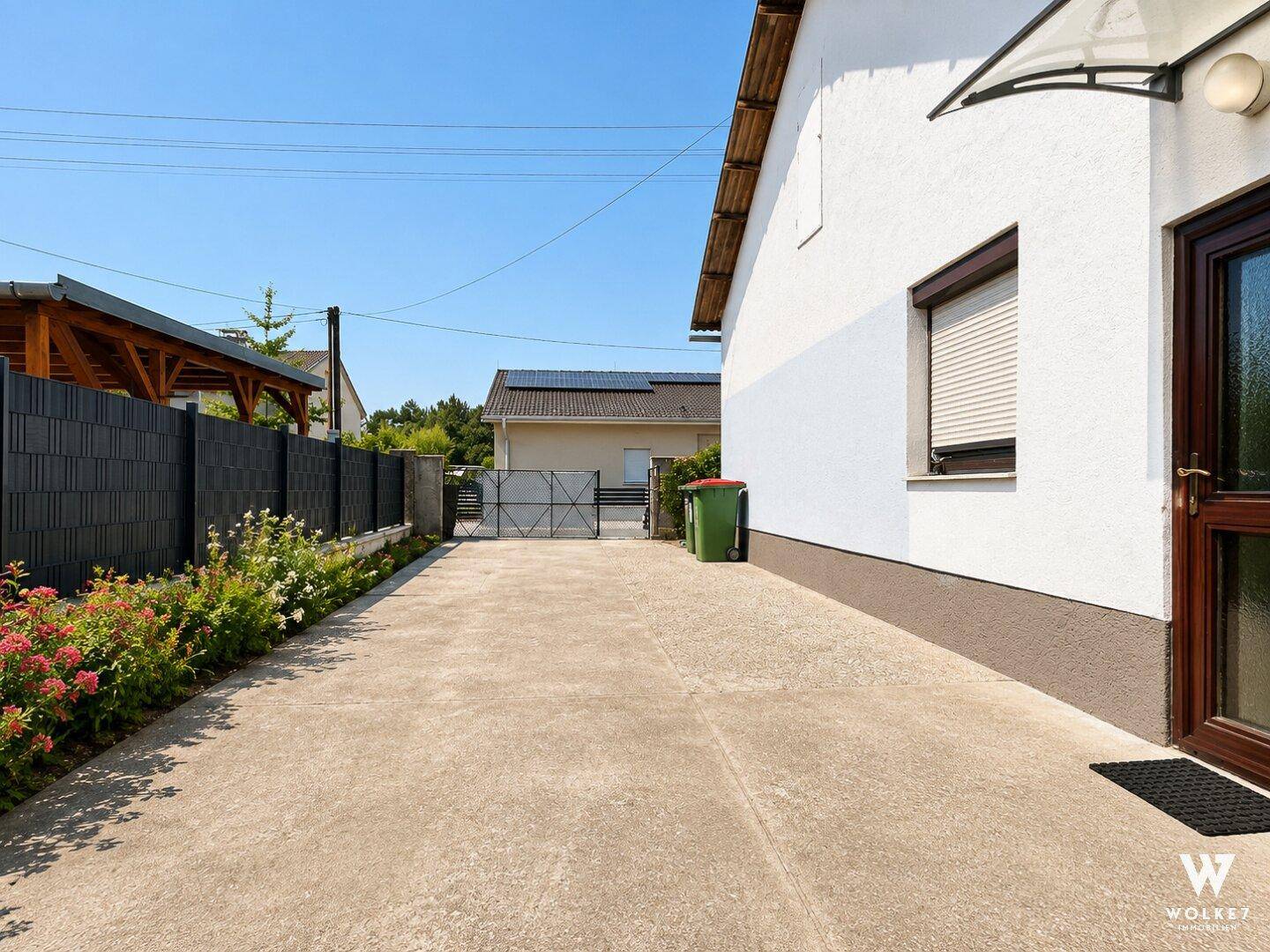 Gepflasterter Zufahrtsbereich neben dem Haus mit Zaun und Tor.