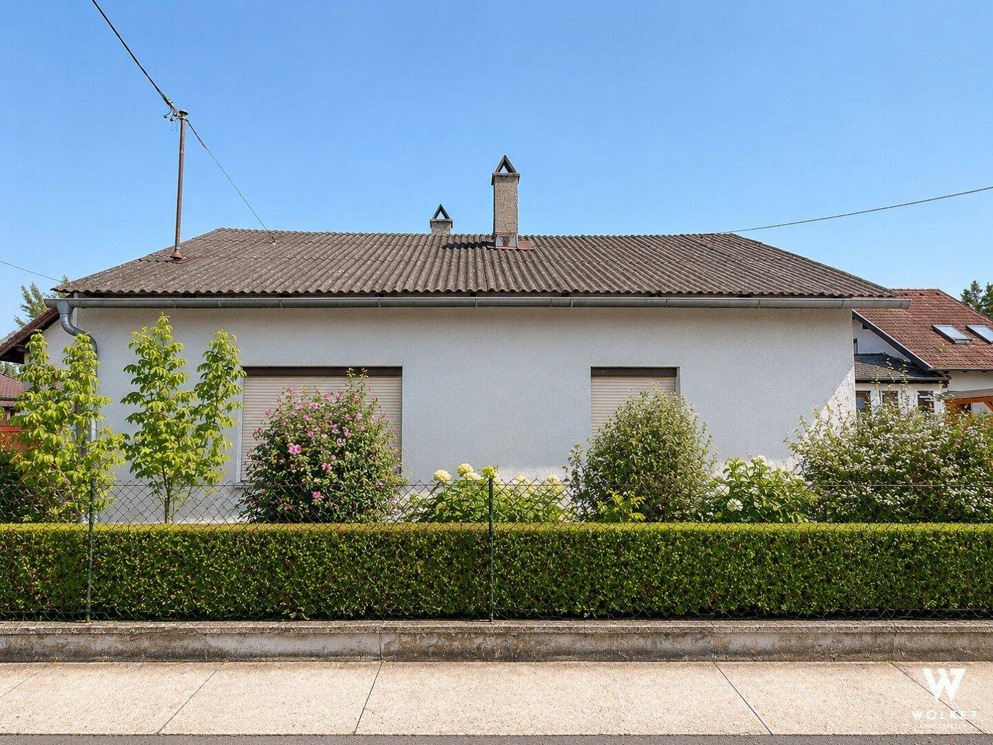 Vorderansicht des Hauses mit weißer Fassade, Ziegeldach und gepflegter Hecke.