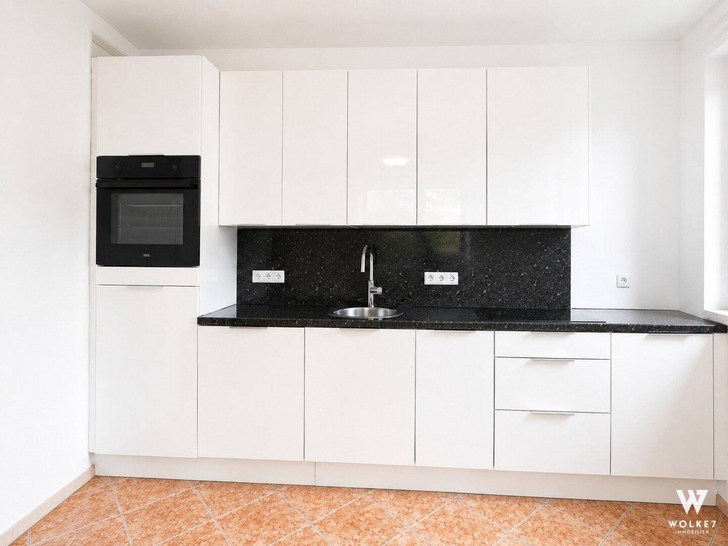 Moderne Küche mit weißen Hochglanzfronten, schwarzer Granitarbeitsplatte und integriertem Backofen.