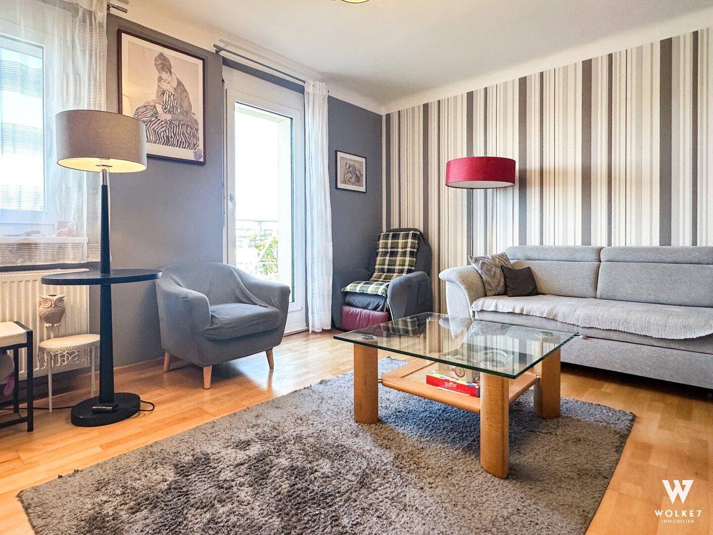 Gemütliches Wohnzimmer mit Sofa, Sesseln, gestreifter Tapete und Zugang zum Balkon.