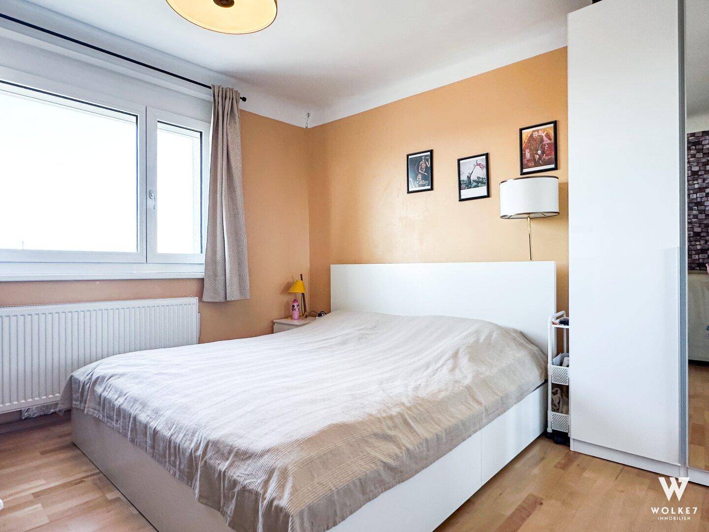 Helles Schlafzimmer mit weißem Bett, hellen Wänden und großem Fenster für viel Tageslicht.