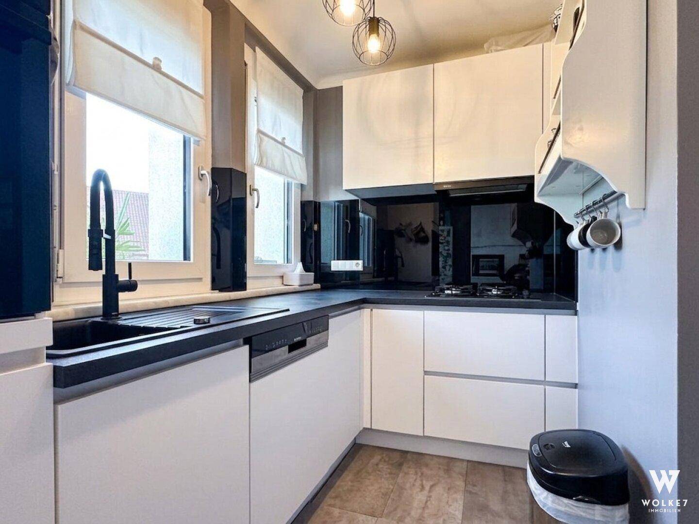Moderne Küche mit weißen Schränken, schwarzer Arbeitsplatte, Spülmaschine und Fenster über der Spüle.