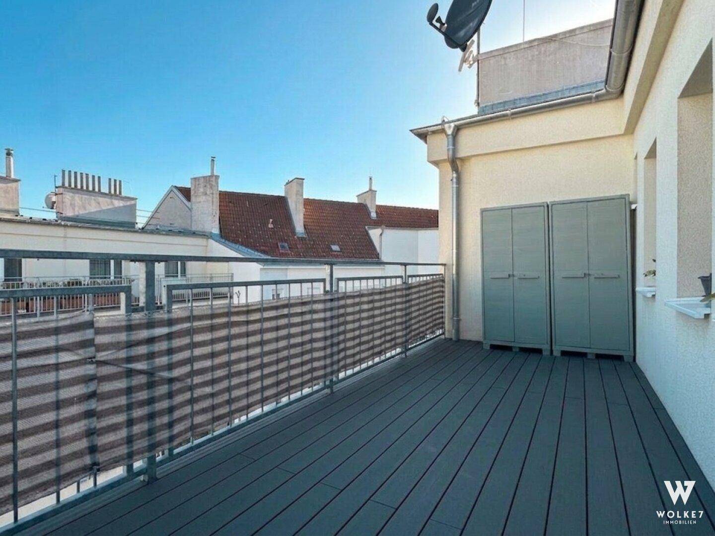Geräumiger Balkon mit Holzboden, Stauraum und Blick auf die umliegenden Dächer der Stadt.