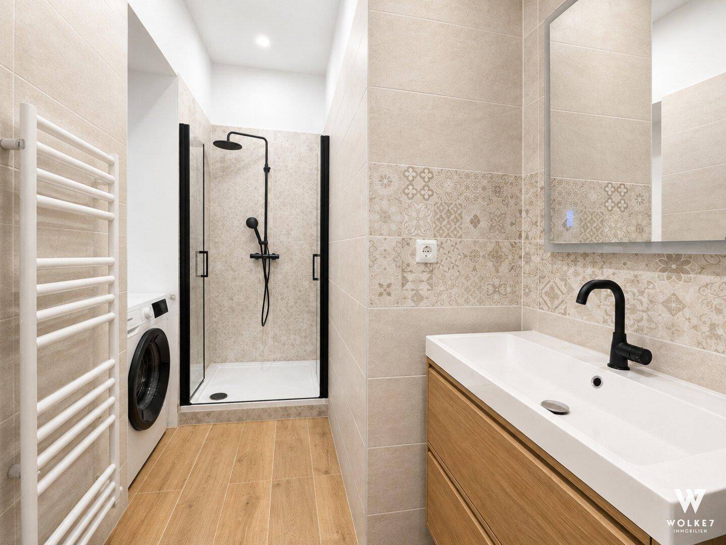 Modernes Badezimmer mit ebenerdiger Dusche, Waschmaschine und beheiztem Handtuchhalter, stilvoll gefliest.