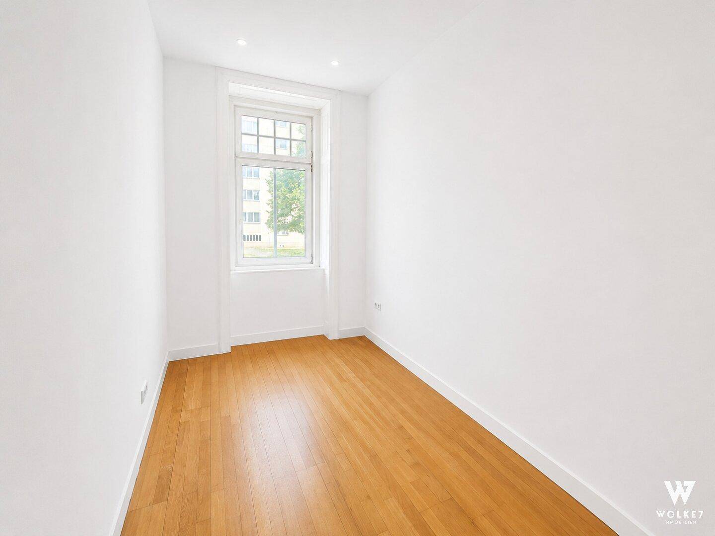 Schmaler, heller Raum mit Holzboden und Fenster, geeignet als kleines Schlafzimmer oder Büro.