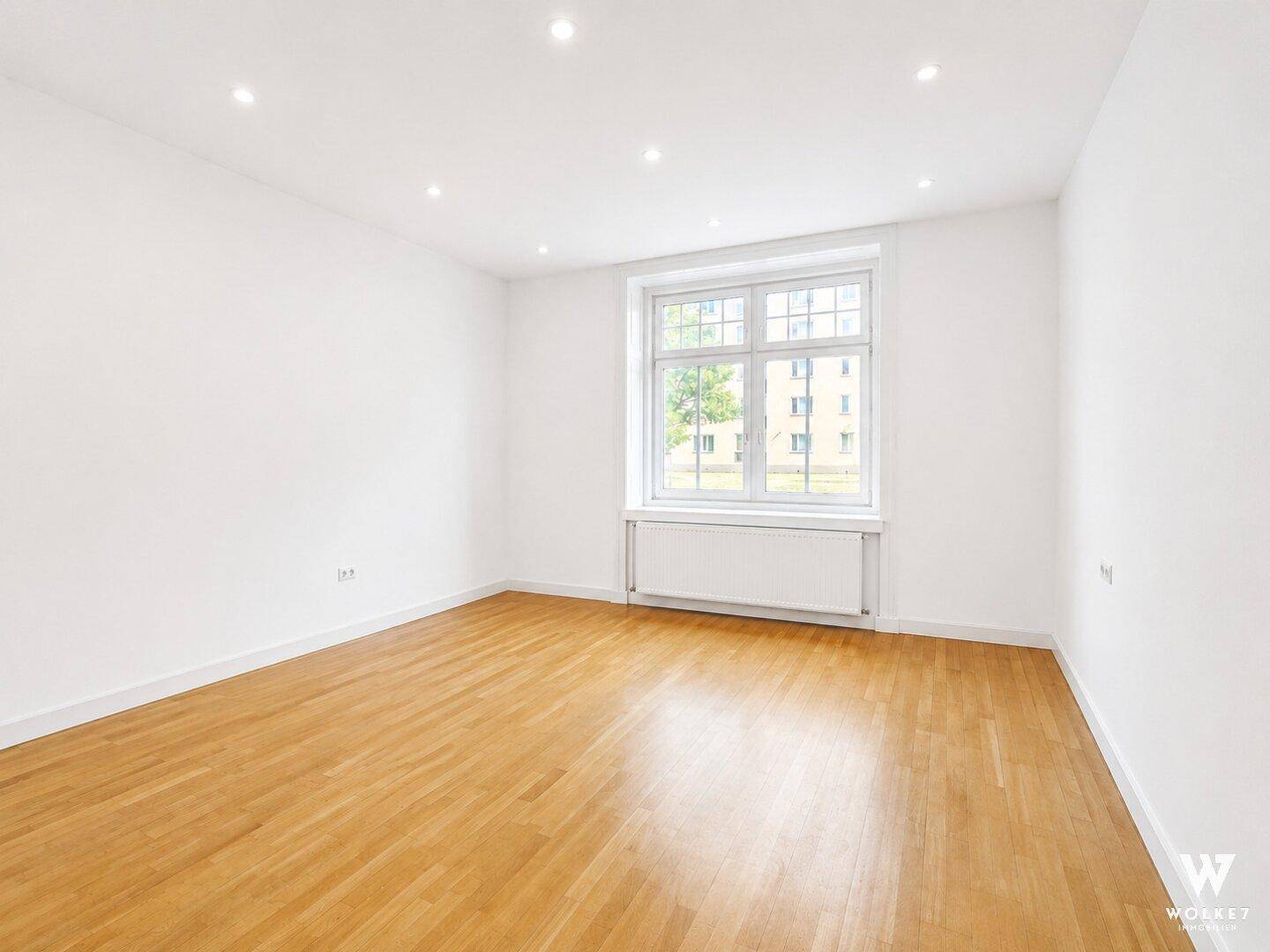 Helles, leeres Zimmer mit Holzboden und großem Fenster, vielseitig nutzbar für Wohnzwecke.