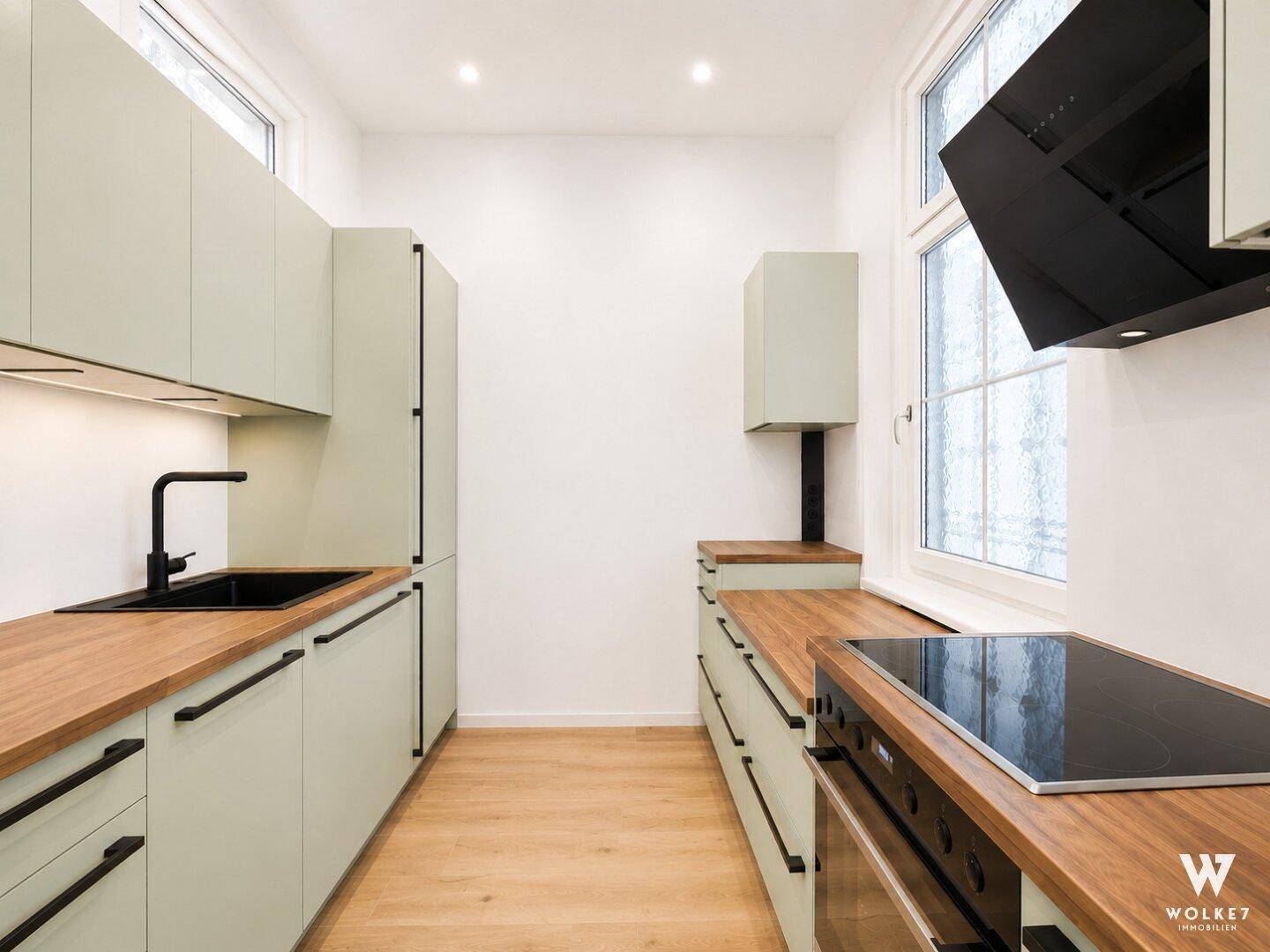 Moderne Küche mit hellgrünen Schränken, Holzarbeitsplatten und Induktionskochfeld, bereit zum Kochen.