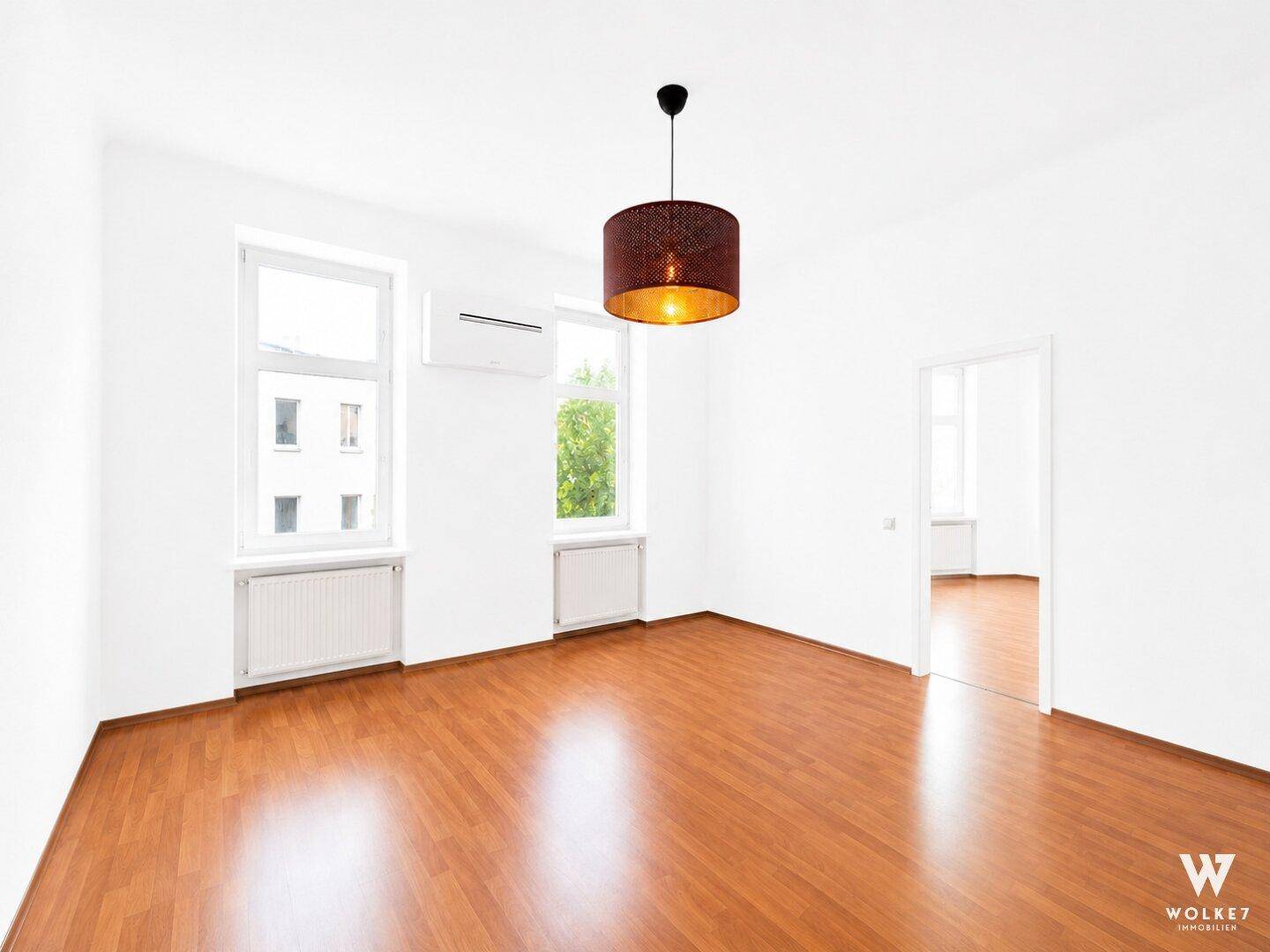Geräumiges, leeres Wohnzimmer mit Parkettboden und großen Fenstern, bereit zur Einrichtung.