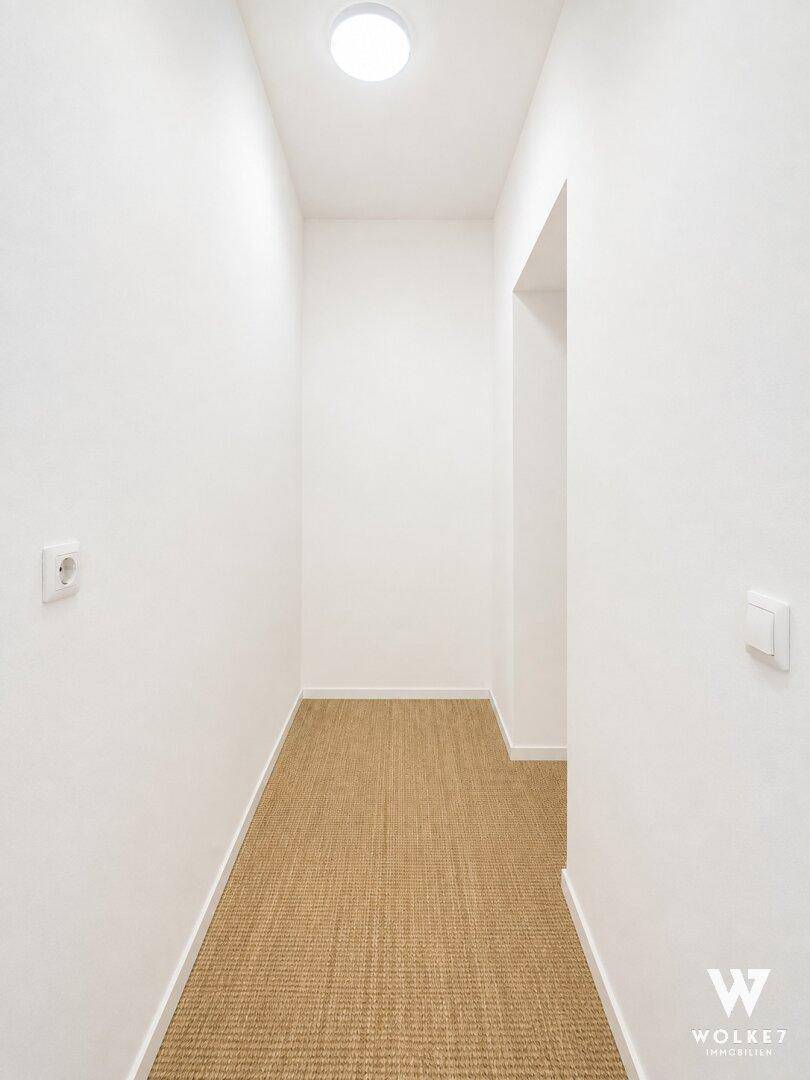 Schmaler Flur mit hellem Teppichboden und weiß gestrichenen Wänden.