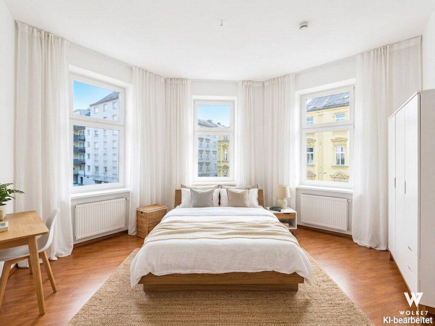 Gemütliches Schlafzimmer mit Holzbett, Parkettboden und drei großen Fenstern.