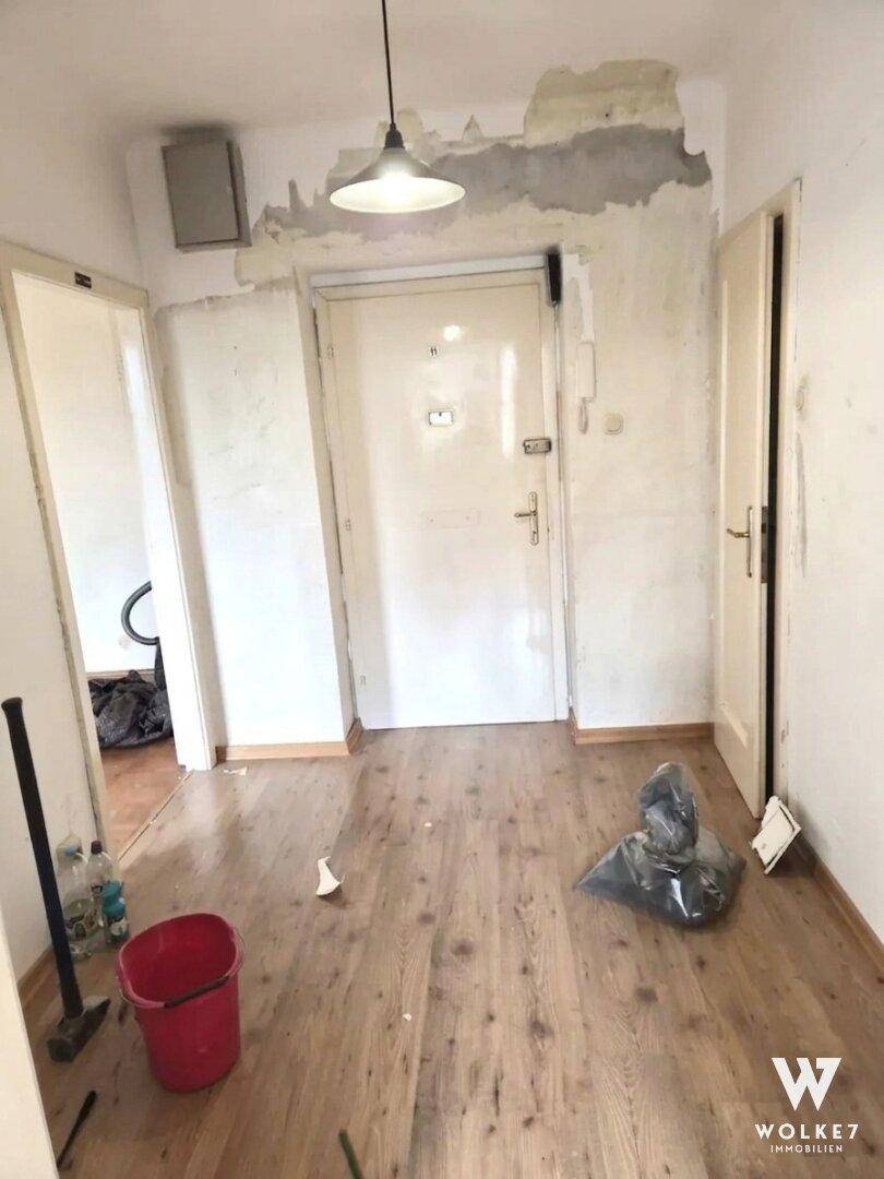 Eingangsbereich im Renovierungszustand mit freigelegten Wänden und Holzboden.