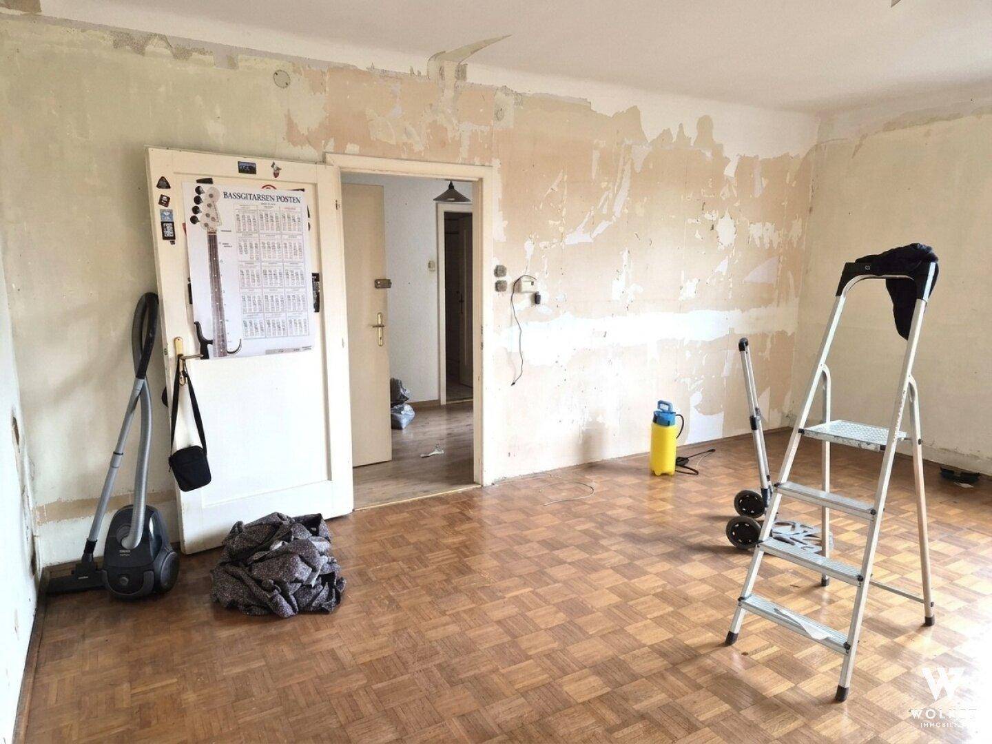 Renovierungsbedürftiger Raum mit abgezogenen Tapeten und Parkettboden.