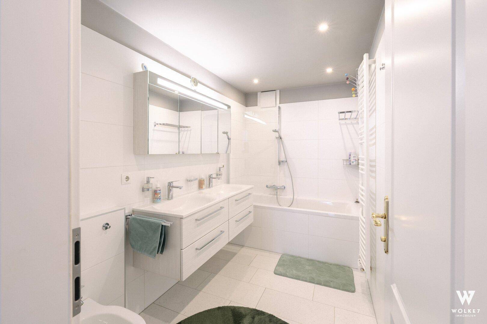 Modernes Badezimmer mit weißen Fliesen, Doppelwaschbecken, Badewanne mit Dusche und Bidet.