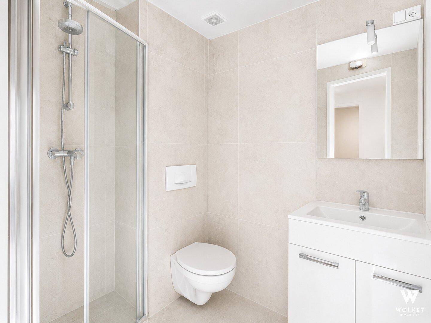 Modernes Badezimmer mit Duschkabine, wandhängendem WC und Waschtisch, hell gefliest.