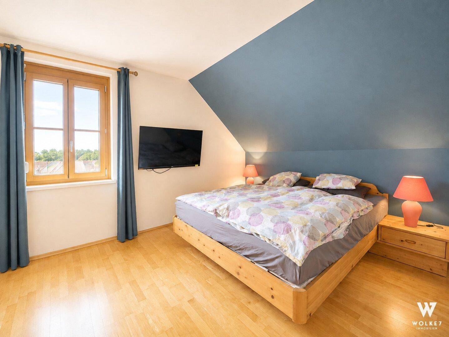 Gemütliches Schlafzimmer mit Holzbett, Dachschräge und Fenster mit weitem Blick in die Landschaft.