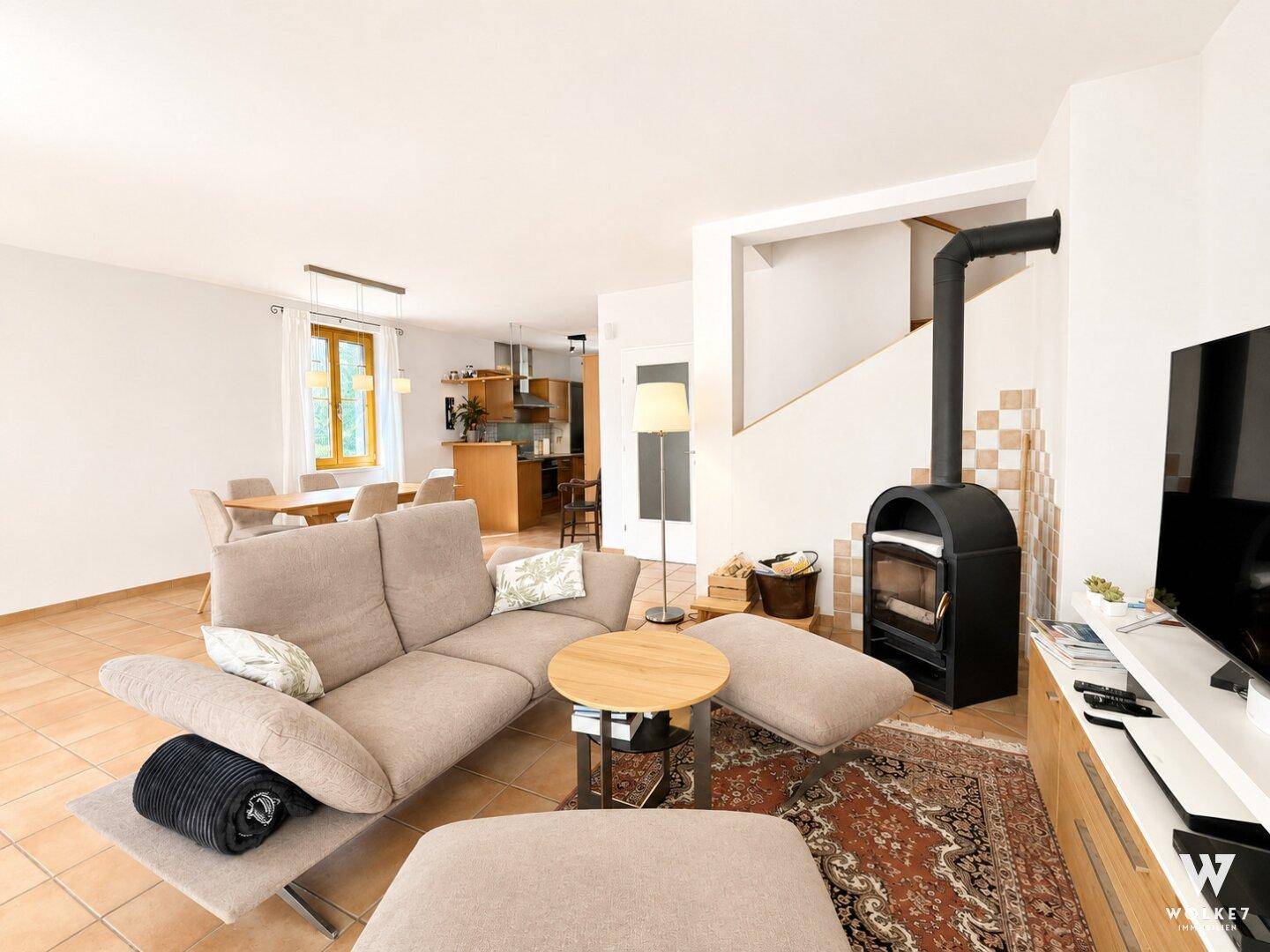 Gemütlicher Wohnbereich mit beigem Sofa, Kaminofen und Blick auf den angrenzenden Essbereich und die Küche.