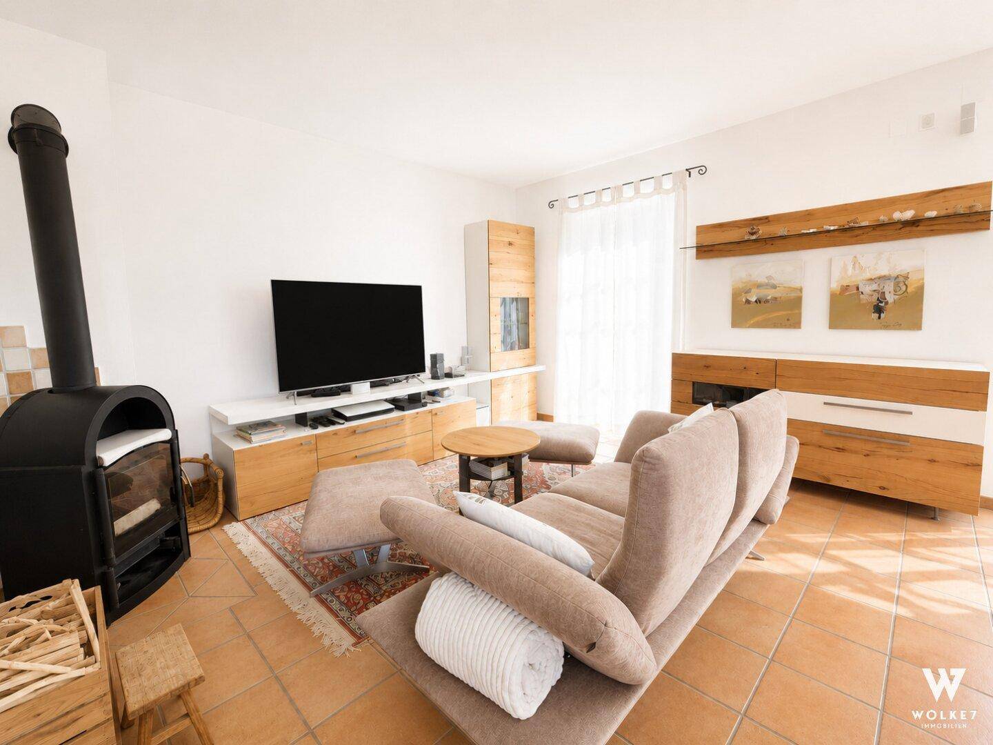 Heller Wohnbereich mit modernem Sofa, Fernseher und stilvollem Kaminofen auf Terrakotta-Fliesenboden.