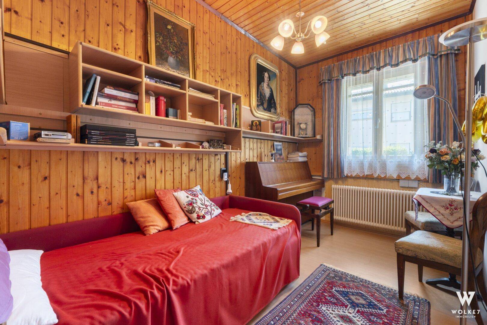 Schlafzimmer mit Holzvertäfelung, Einzelbett und Schreibtischbereich.