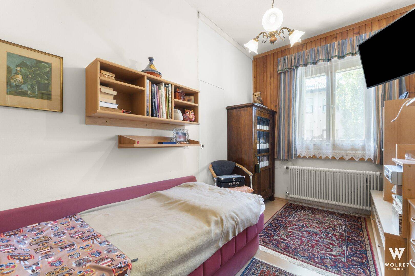 Schlafzimmer mit Holzvertäfelung, Einzelbett und Bücherregal.
