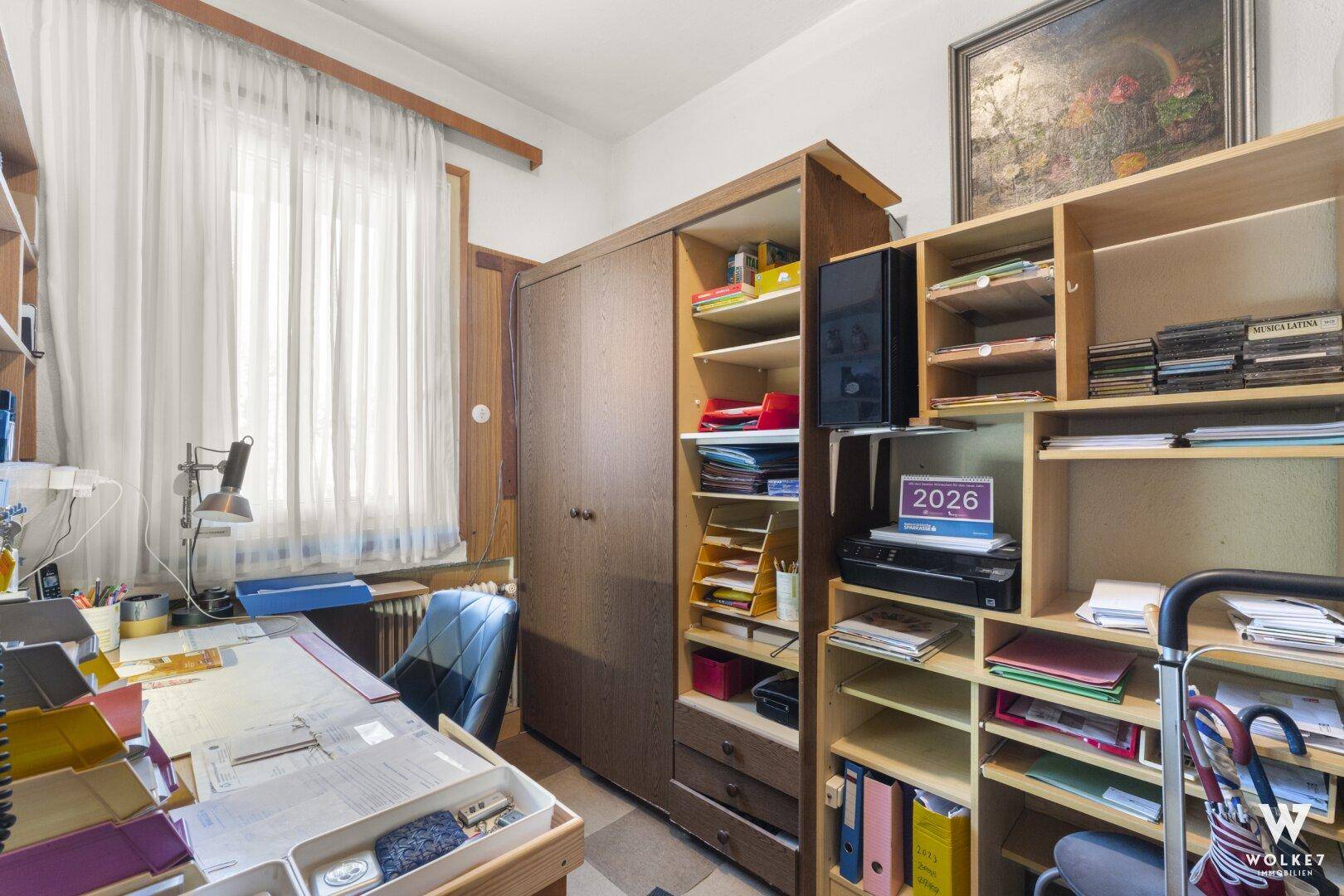 Arbeitszimmer mit großem Schreibtisch, Regalen und Fenster.