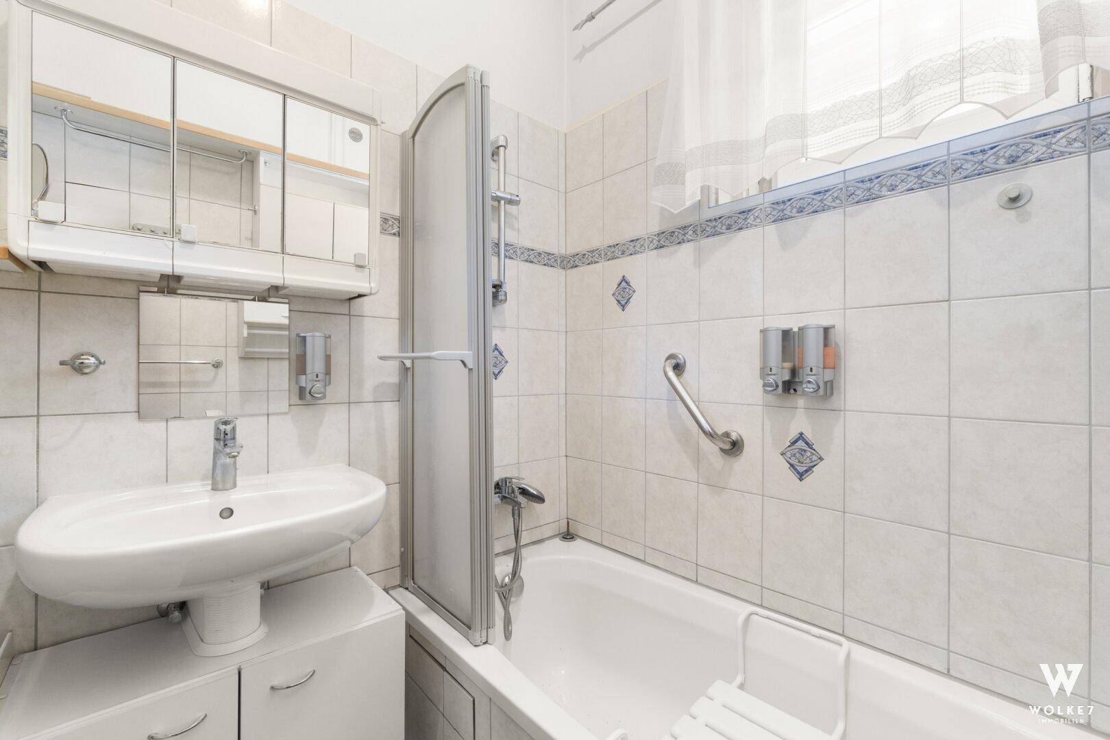 Badezimmer mit Badewanne, Duschabtrennung, Waschbecken und Fenster.