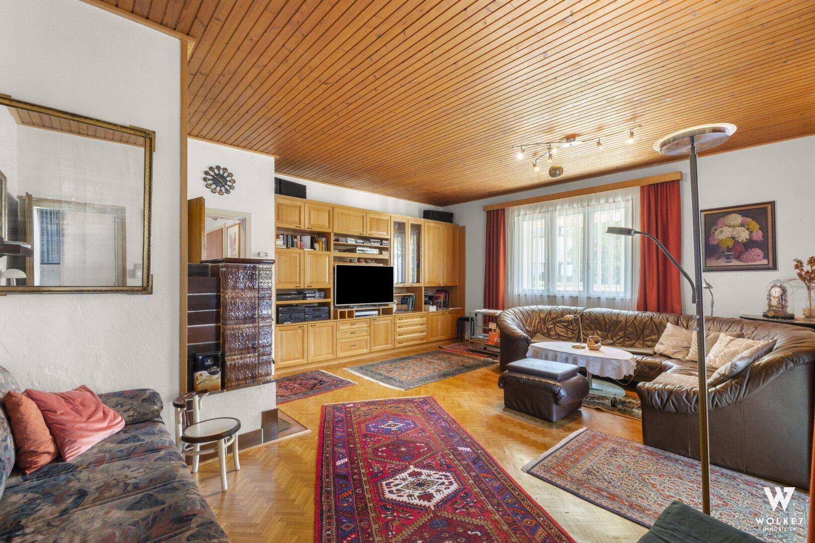Geräumiges Wohnzimmer mit Holzbalkendecke, Kachelofen und bequemen Sofas.