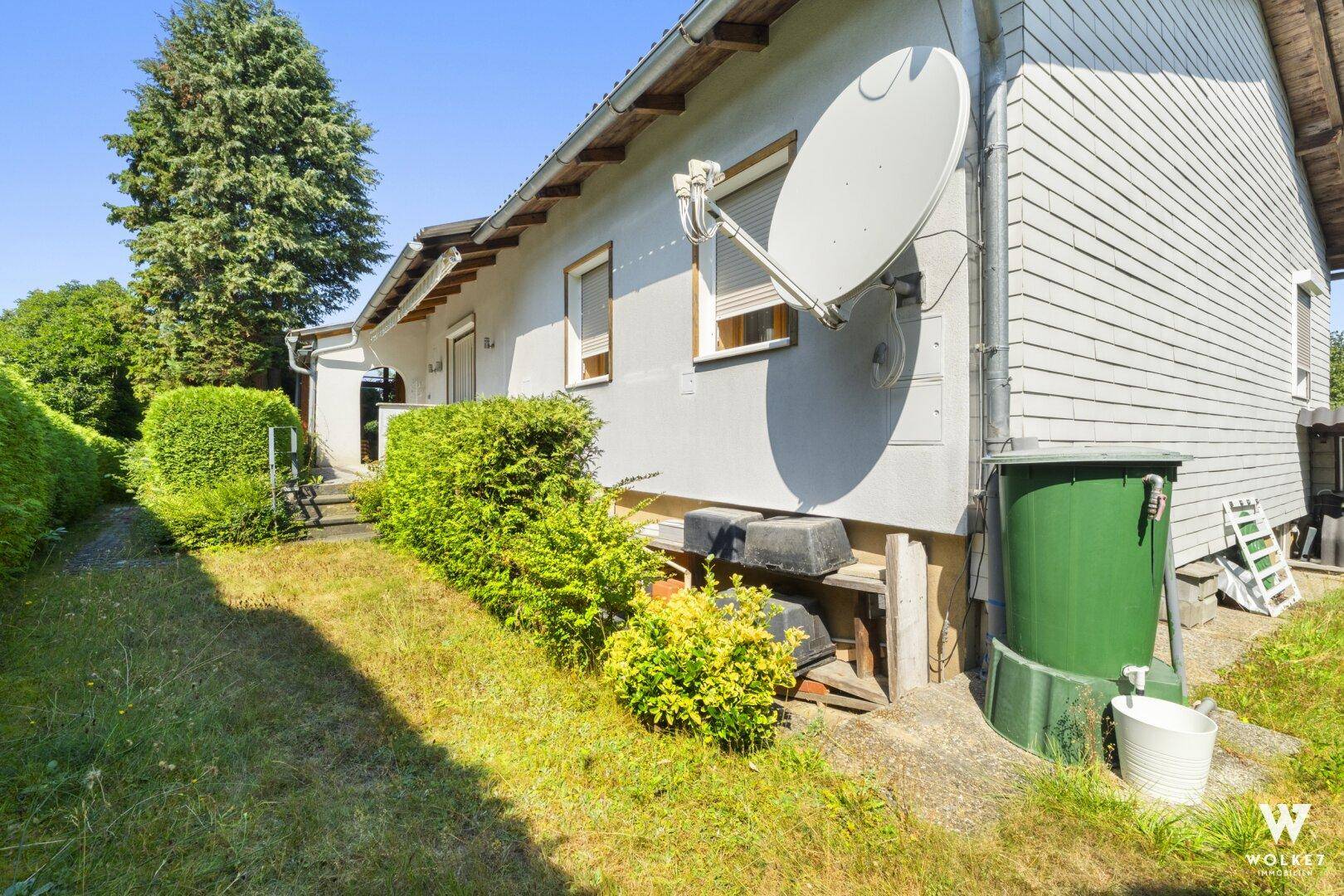 Seitenansicht des Hauses mit Garten, Hecke und Satellitenschüssel.