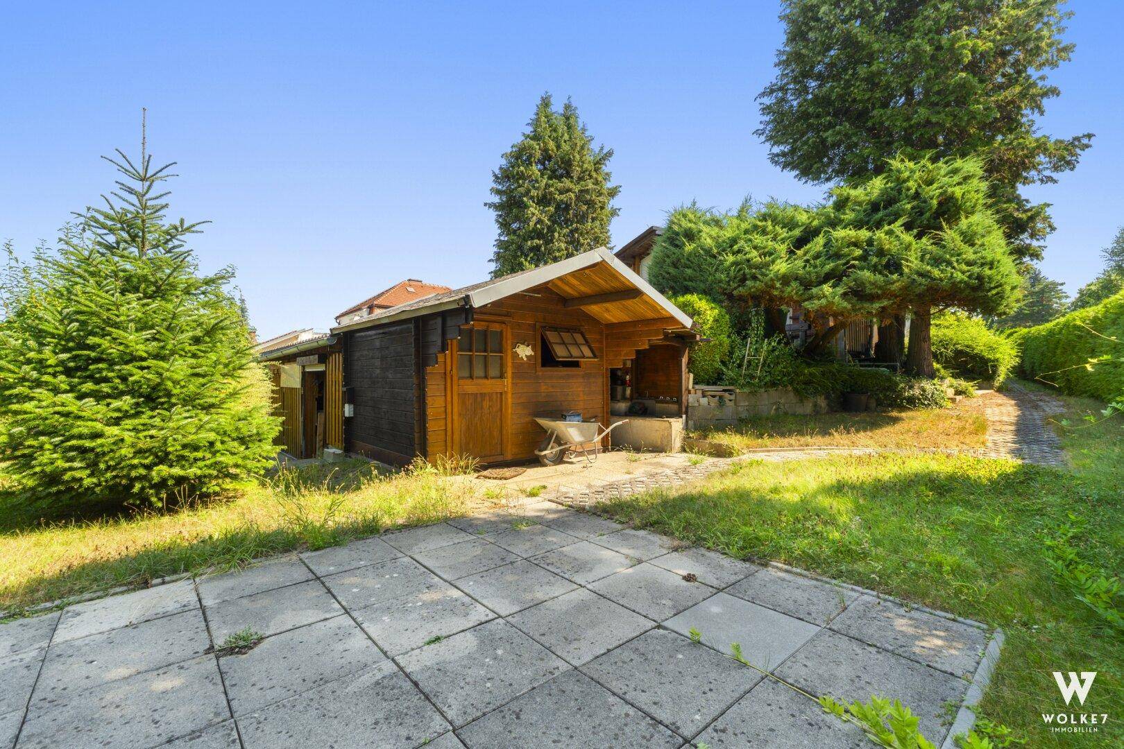 Kleines Holzgartenhaus mit gepflastertem Bereich im Grünen.