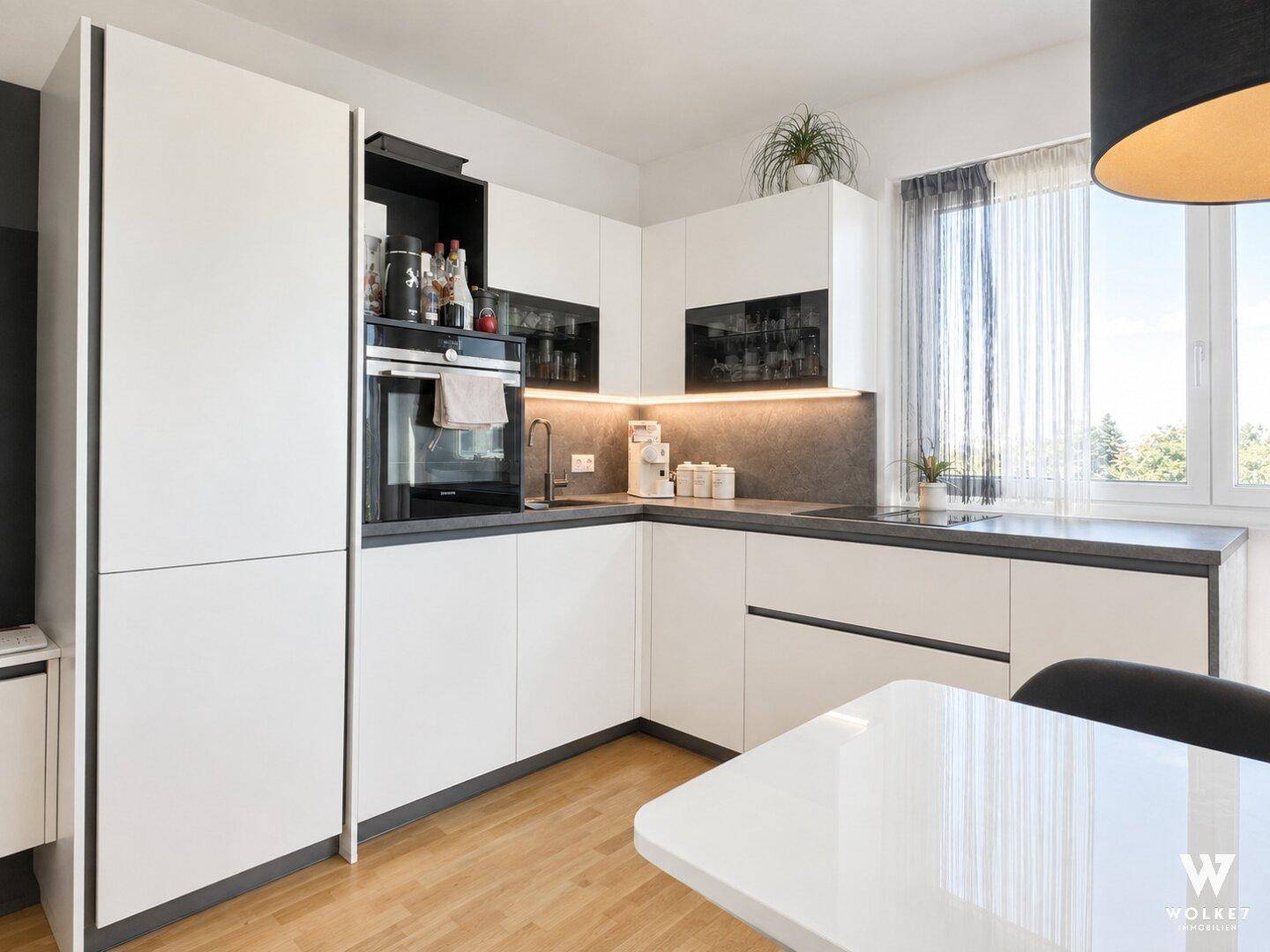 Moderne Einbauküche mit weißen Schränken, dunkler Arbeitsplatte und großem Fenster.
