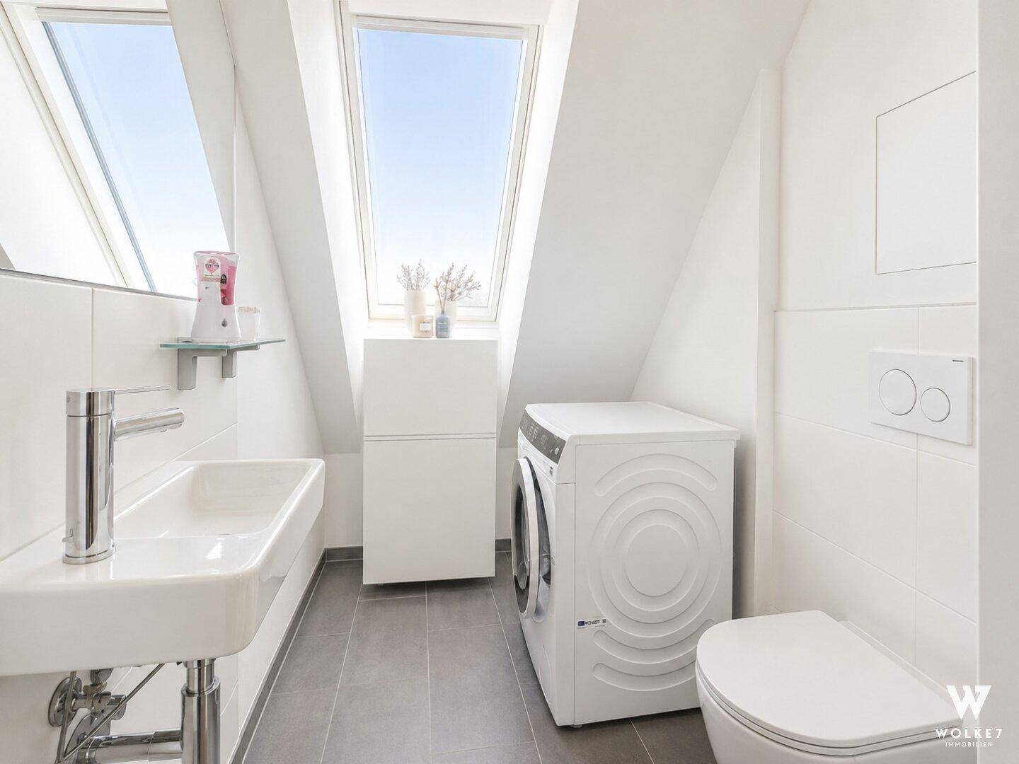 Modernes WC im Dachgeschoss mit Waschmaschine, Waschbecken und Dachfenster.