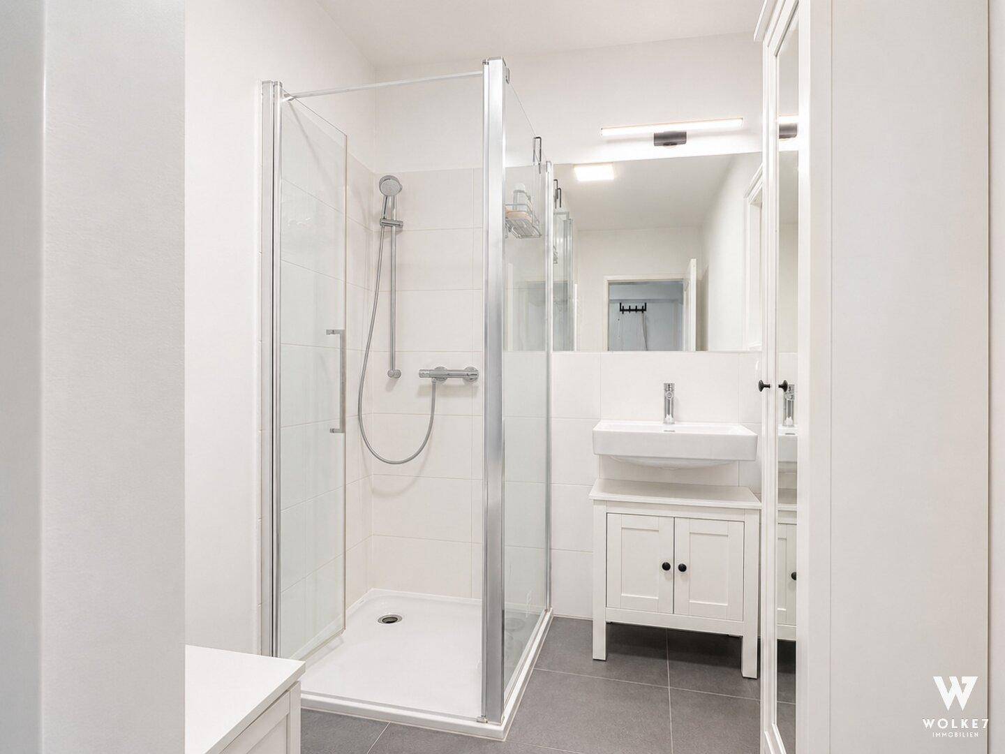 Modernes Badezimmer mit Duschkabine, Waschbecken und grauen Bodenfliesen.