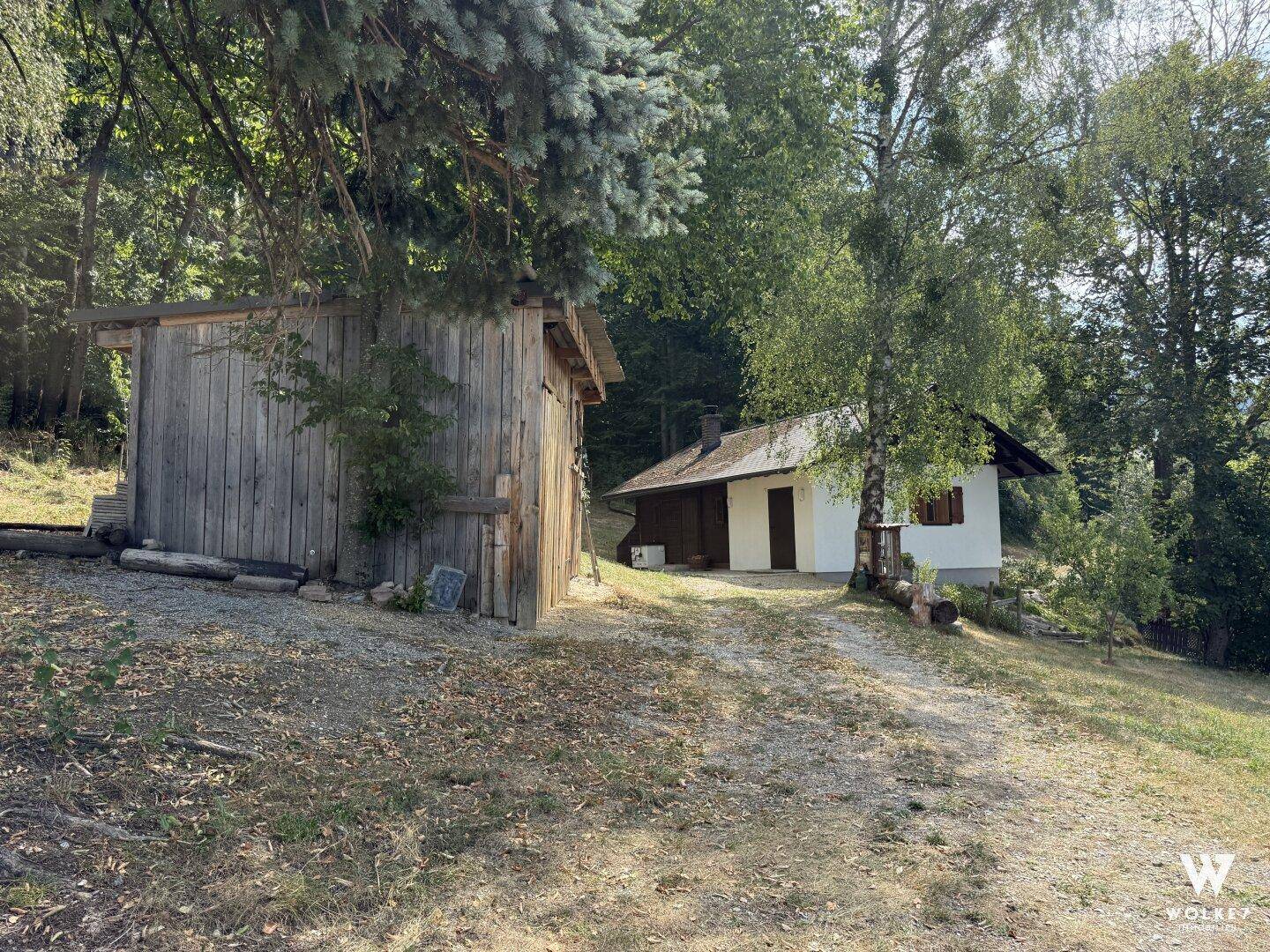 Landhaus mit weißer Fassade und Holzschuppen, umgeben von Bäumen und Natur.