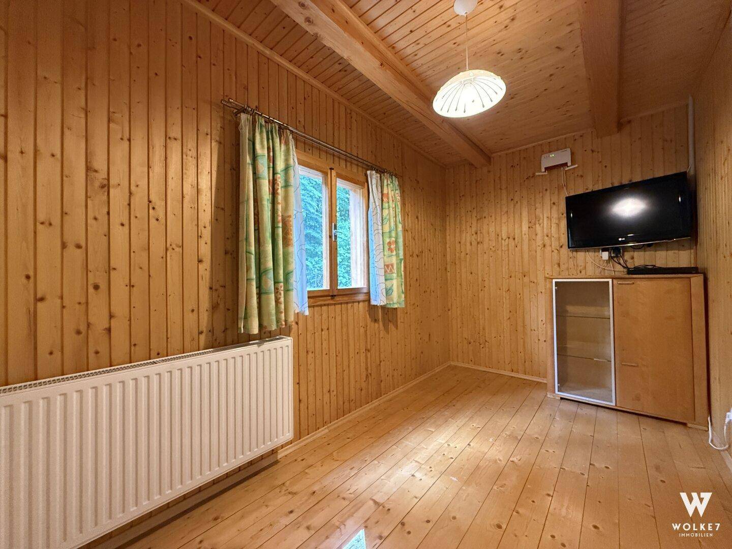 Wohnraum mit Holzwänden, Holzboden, Fenster und Heizkörper.