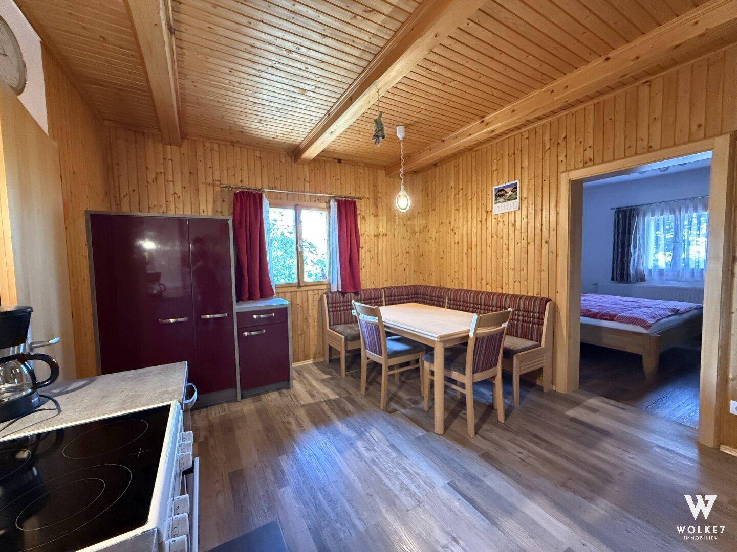 Offener Küchen- und Essbereich mit Holzwänden und Blick in ein angrenzendes Schlafzimmer.