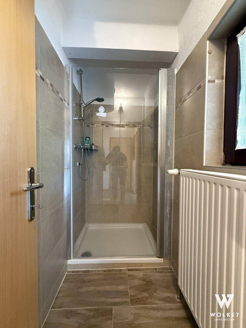 Badezimmer mit Duschkabine, Fliesenboden und Heizkörper.