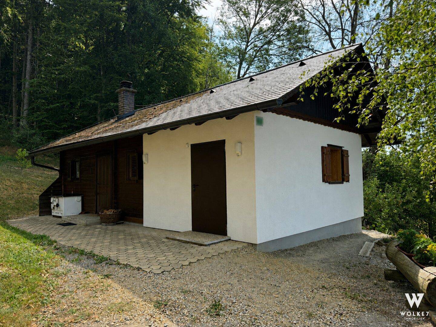 Seitenansicht eines charmanten Hauses mit weißer Fassade und Holzverkleidung in grüner Umgebung.