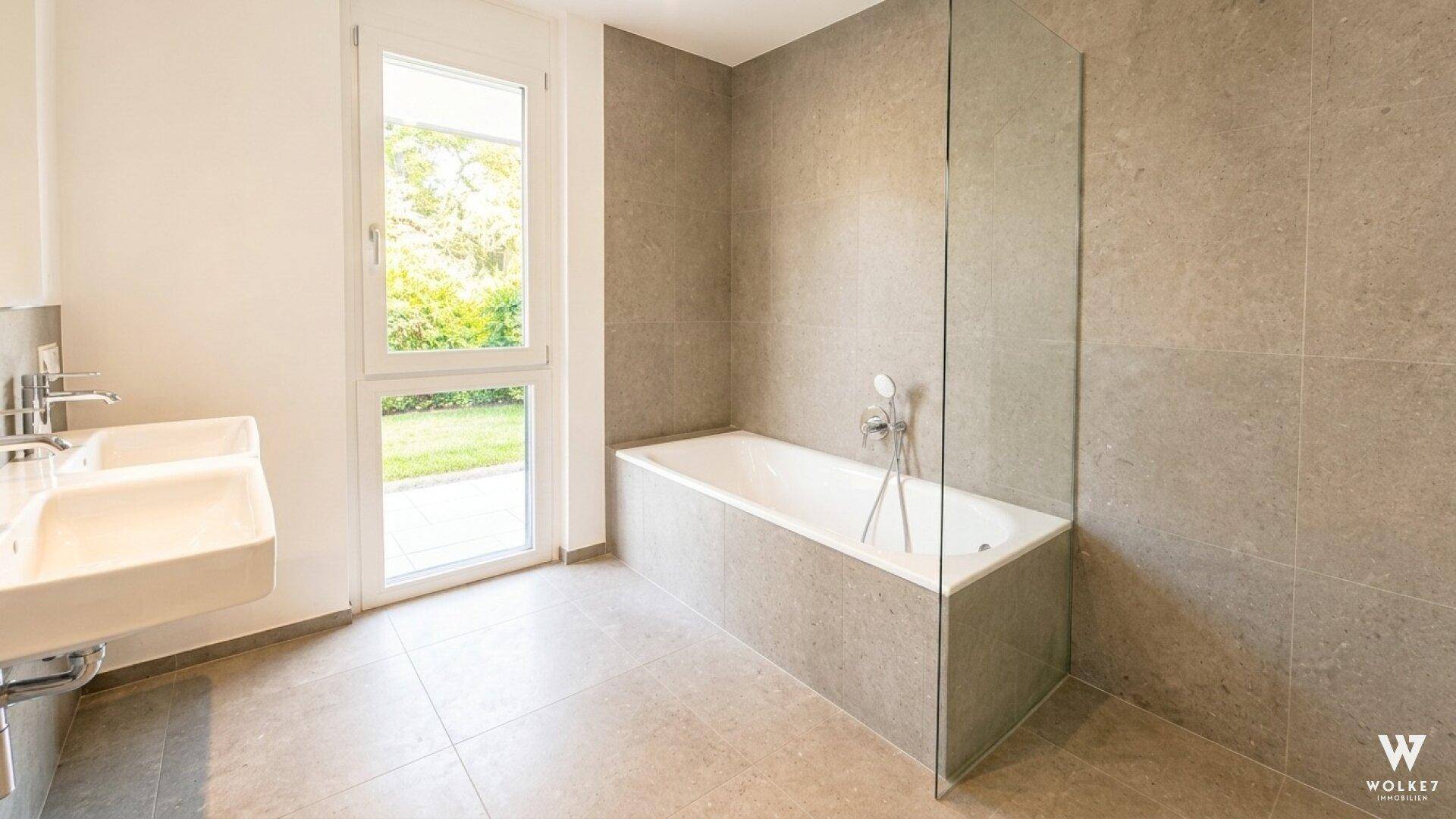 Modernes Badezimmer mit Badewanne, Doppelwaschbecken und Fenster mit Blick ins Grüne.