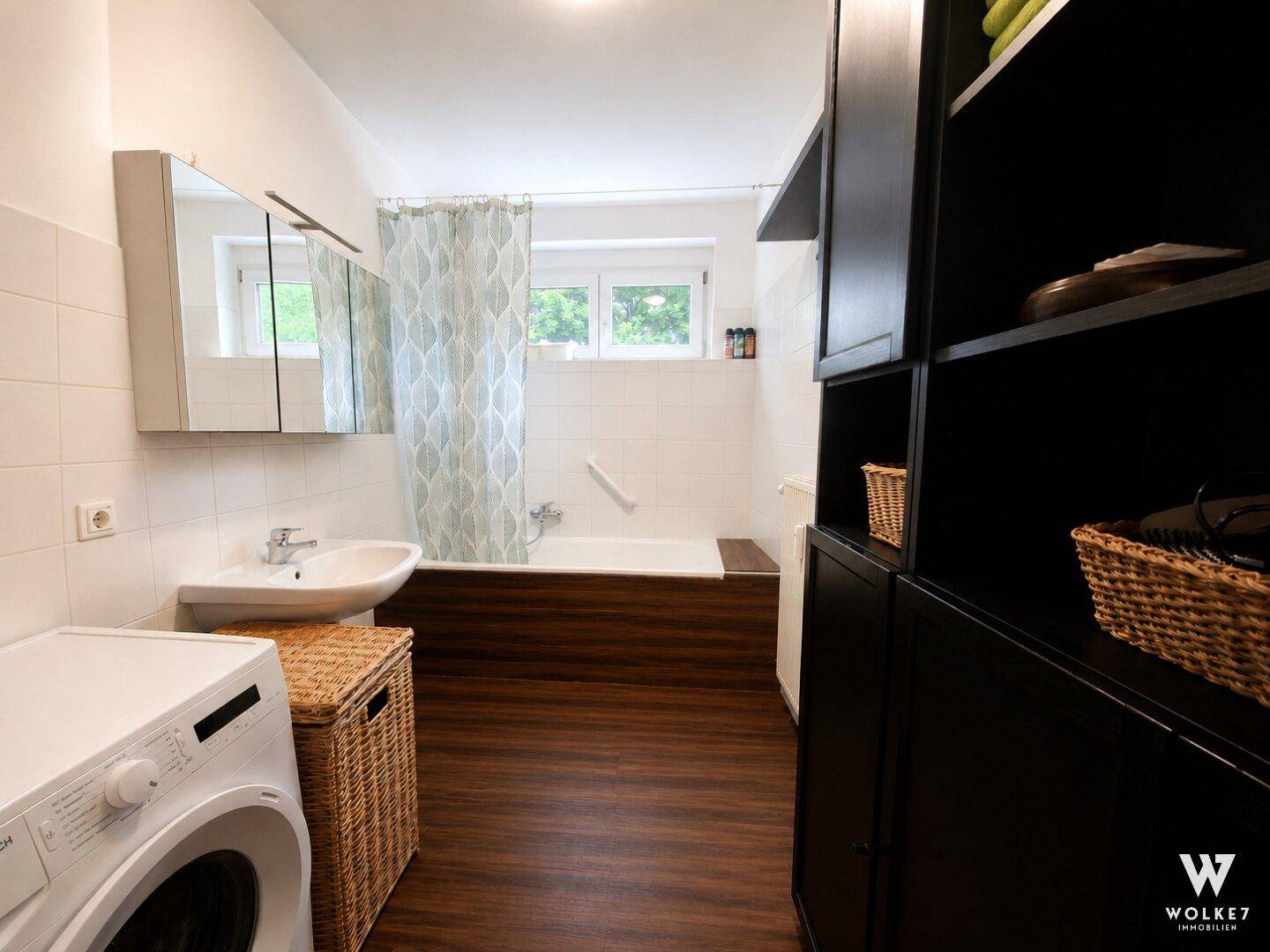 Badezimmer mit Badewanne, Duschvorhang, Waschbecken und Waschmaschine unter dem Fenster.