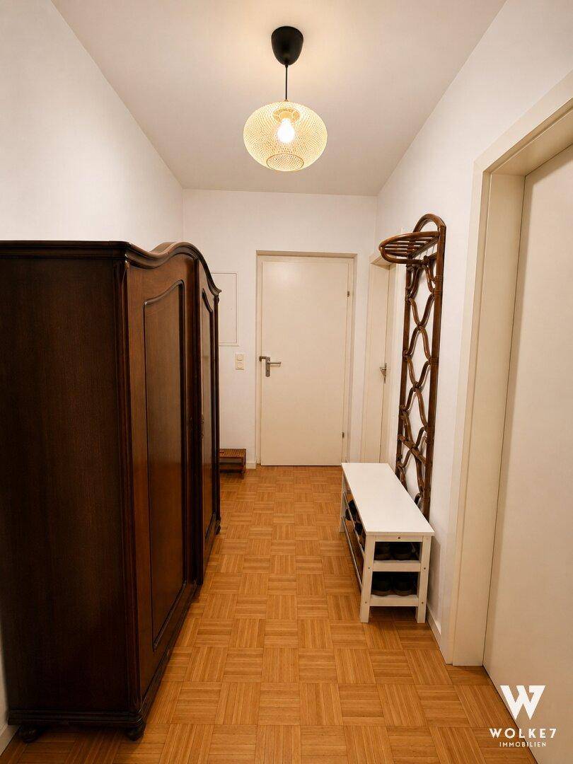 Heller Eingangsbereich mit dunklem Holzschrank, Schuhbank und Parkettboden.