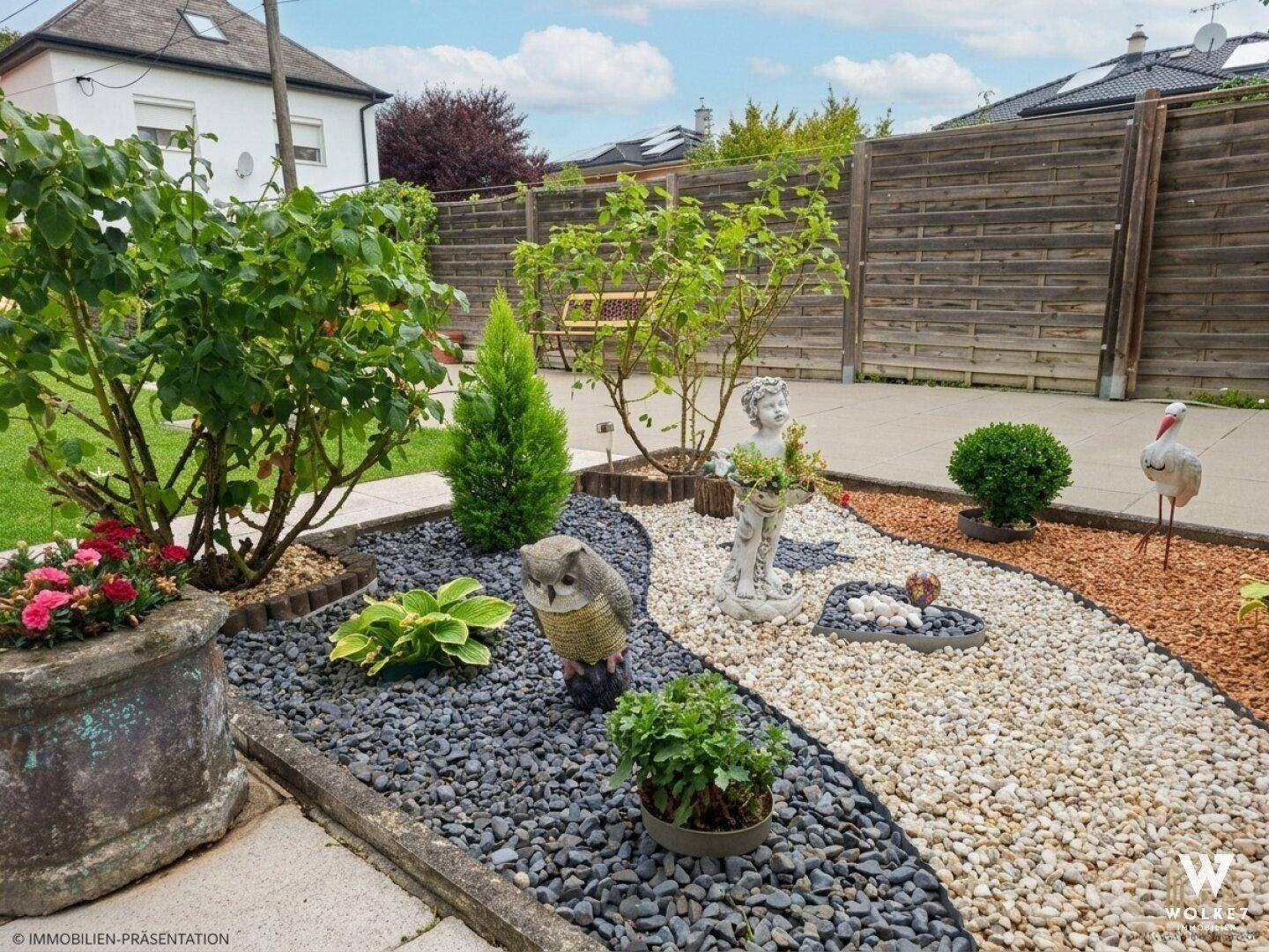Dekorativer Gartenbereich mit Kiesbeeten, Pflanzen und kleinen Statuen.