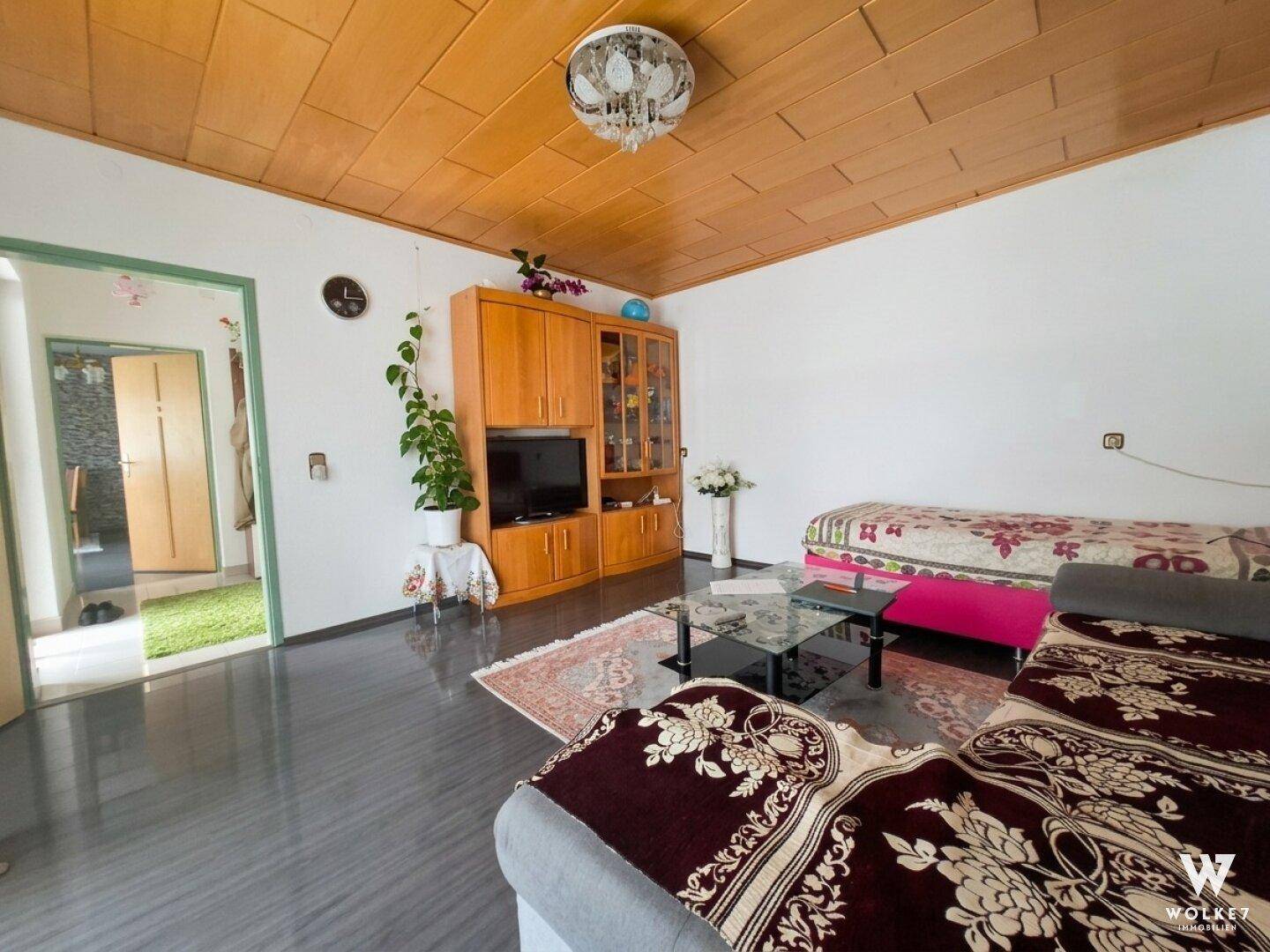 Gemütliches Wohnzimmer mit Holzdecke, dunklem Boden und traditionellen Möbeln.