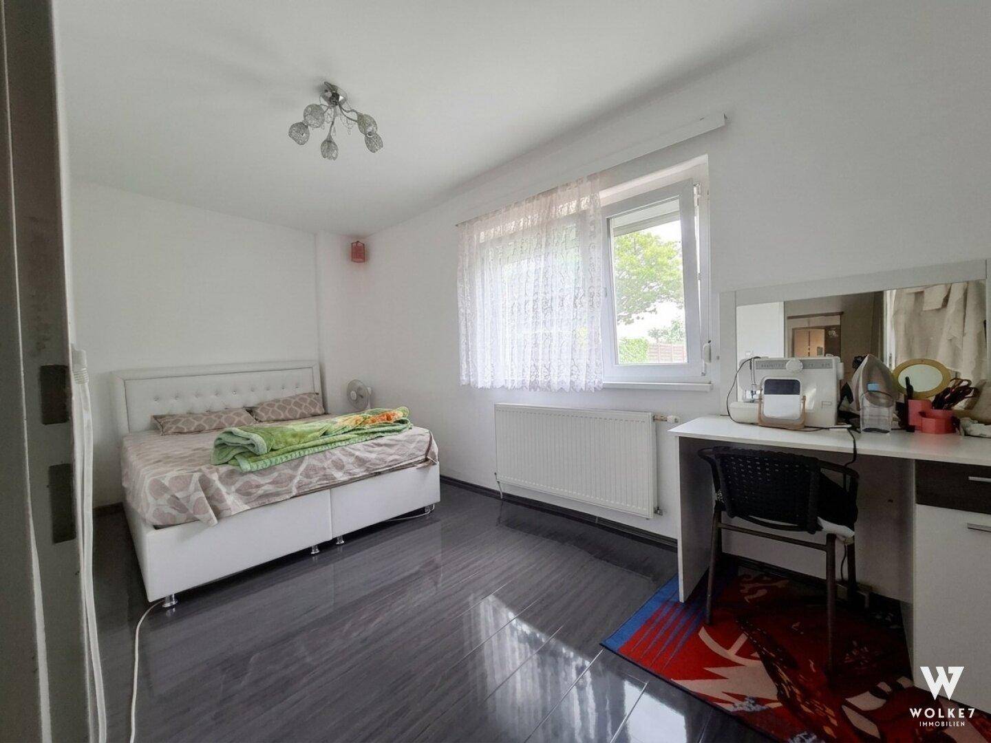 Helles Schlafzimmer mit Doppelbett, Schreibtisch und dunklem Laminatboden.